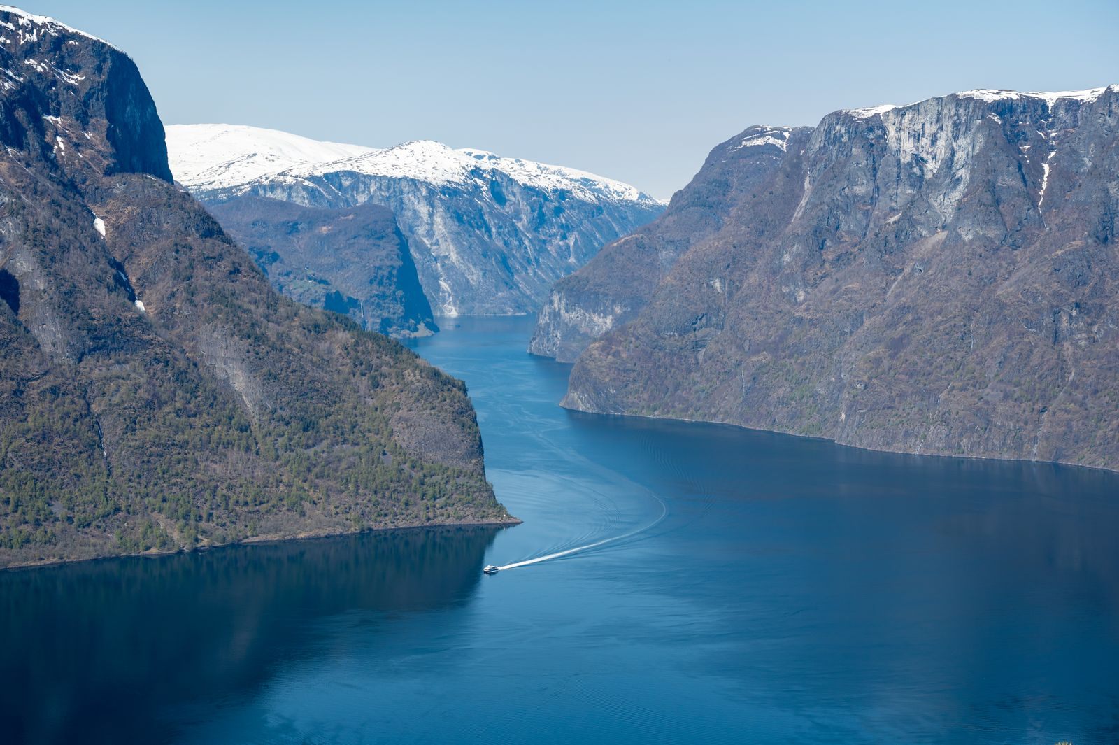 A boat crossing the deep blue Aurlandsfjord between steep cliffs and snowy peaks, one of the Norway fjords near Flam