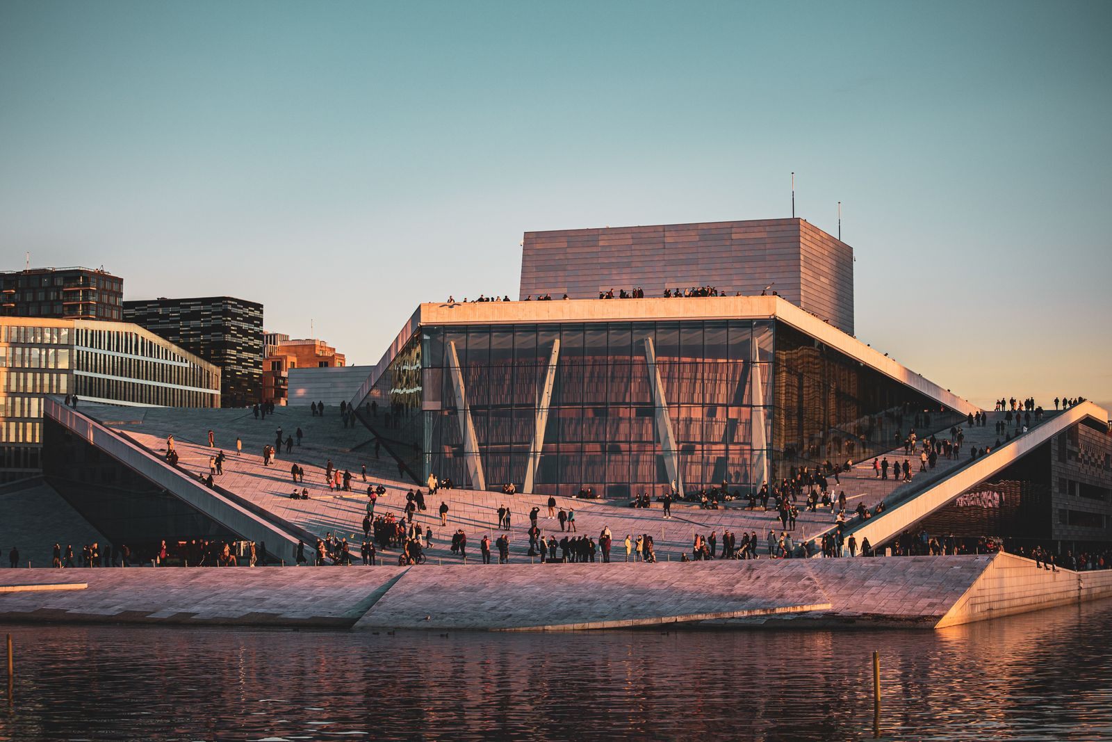 People walking on the sloping roof of the Oslo Opera House at sunset, one of the top things to do in Norway