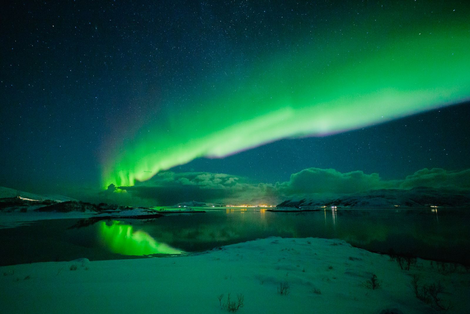 Green northern lights over a snowy fjord shore near Tromso, at the best time of year for the northern lights in Norway